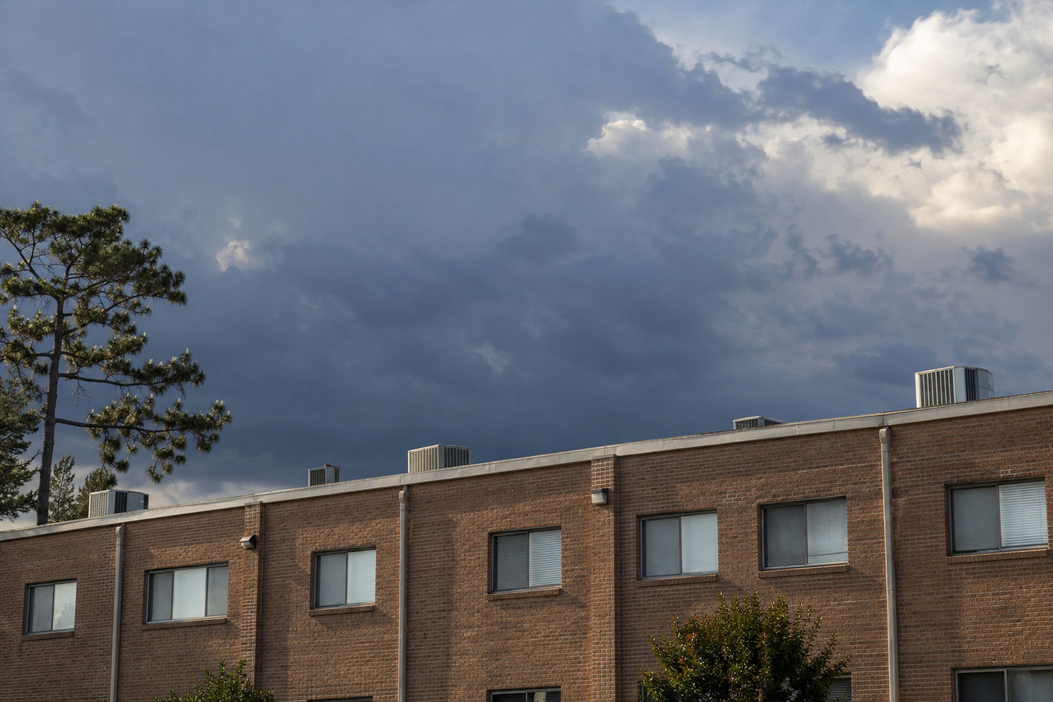 Parapet line and rooftop units of a low-rise brick apartment building under a hazy sky