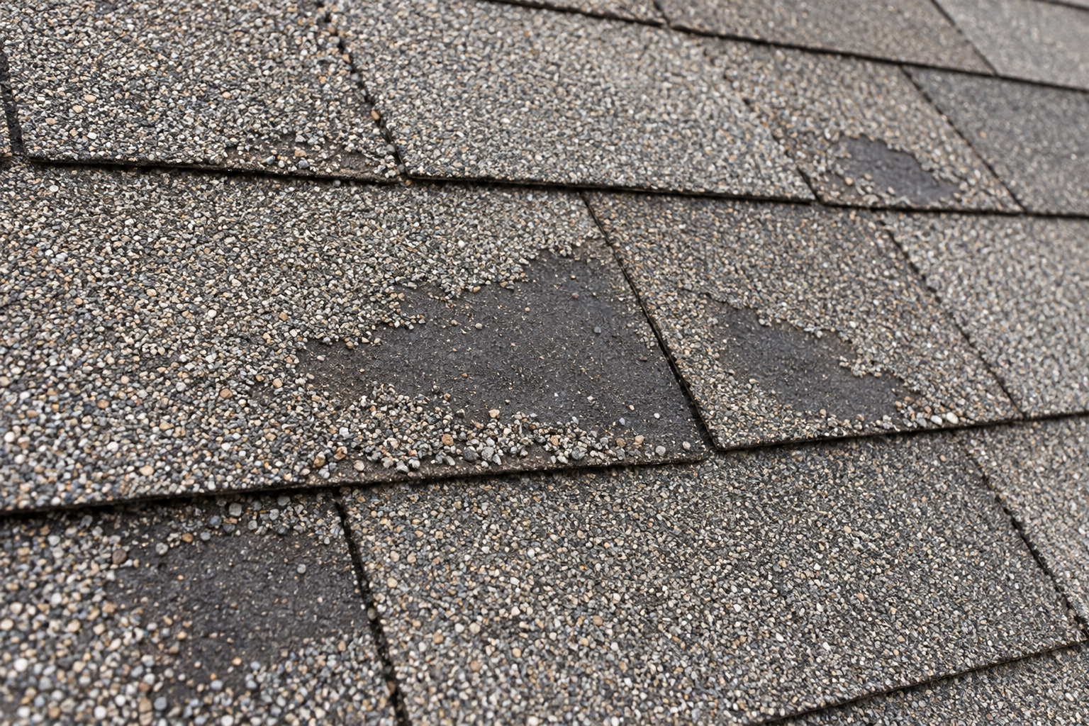 Close view of asphalt shingles with bald patches where the granules have worn away