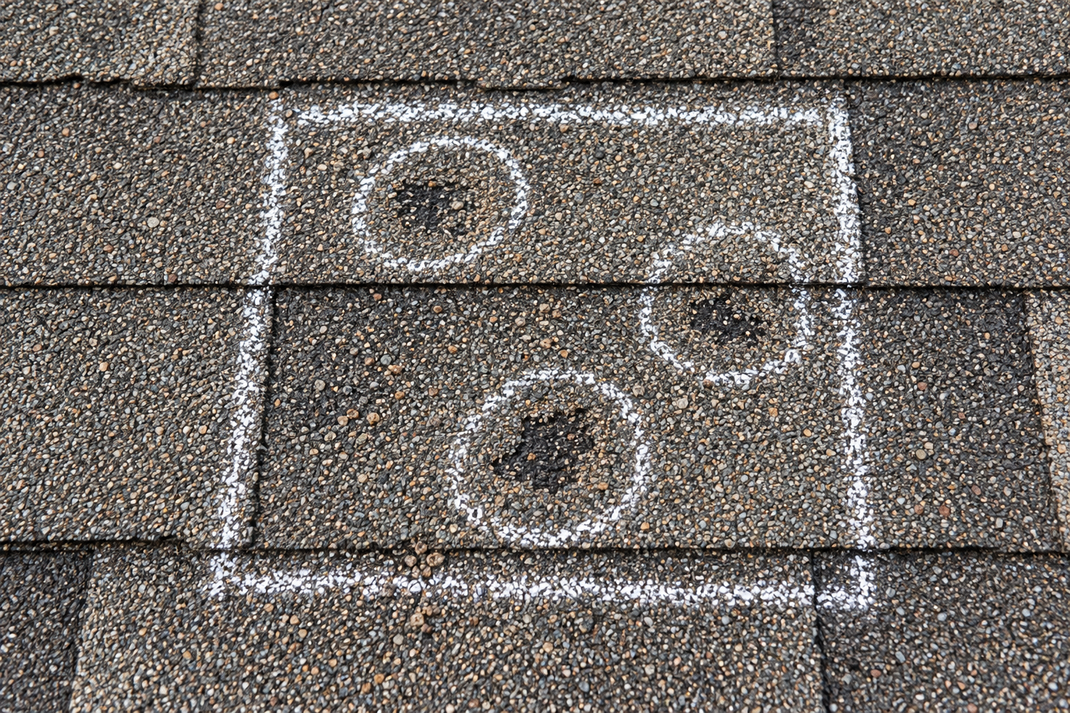Top-down view of a chalk-outlined test square on asphalt shingles with each hail hit circled in chalk