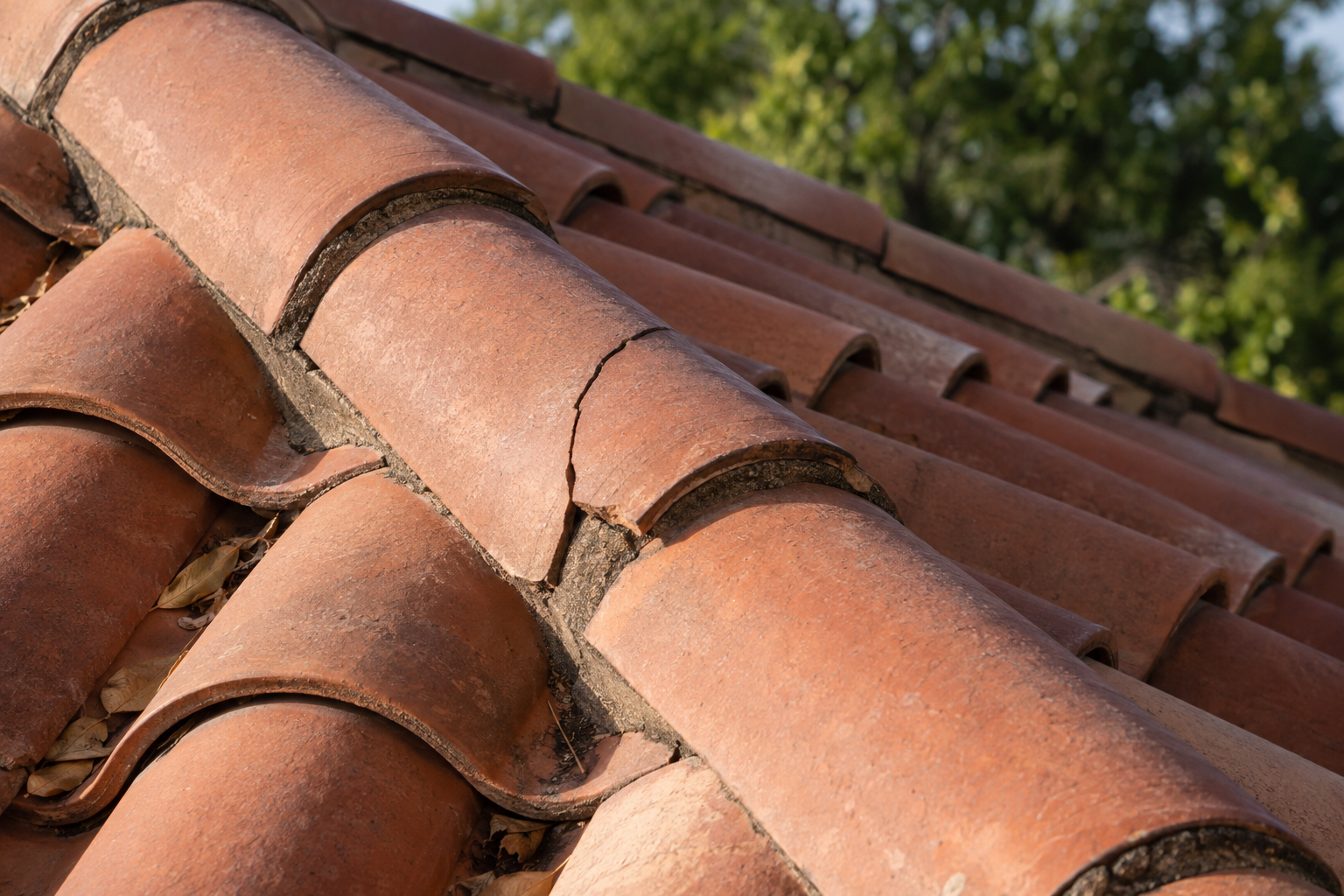 A cracked clay roof tile beside sound tiles along the hip of a tile roof